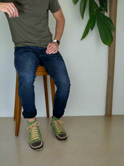 Person sitting on a chair with legs extended, wearing green shoes and blue jeans, against a white wall.